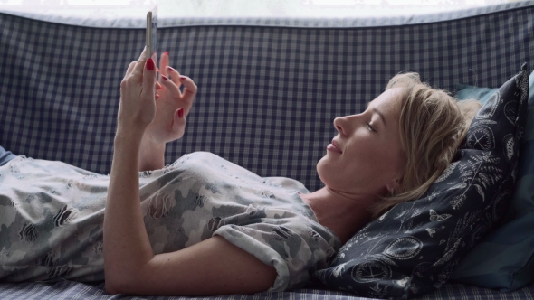 Happy Woman Using Smartphone on Sofa at Home