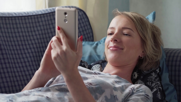 Happy Caucasian Woman Lying on Sofa at Home and Using Smartphone