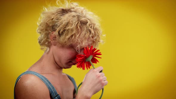 Side View of Young Romantic Queer Man Smelling Red Flower Touching Neck with Petals alt