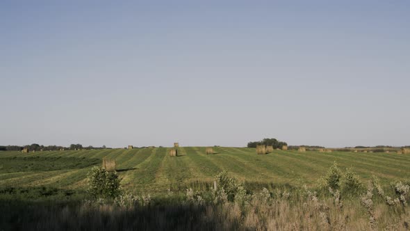 Pan left to right of hay bails in field behind wire fence in Manitoba alt
