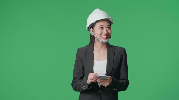 Asian Female Engineer Using Smartphone And Looking Around While Walking In The Green Screen Studio alt