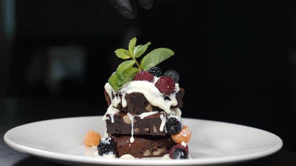 Stack of Brownies Dessert Being Decorated with Berries on White Plate. Falling Berries in Slow alt