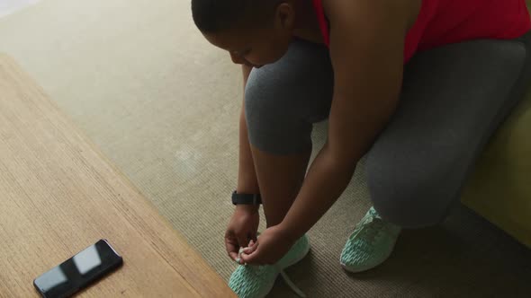 African american plus size woman practicing yoga, tying shoelaces in living room alt