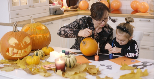 Woman and Girl Painting Face on Pumpkin alt