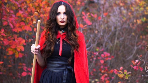 Young Gorgeous Brunette Witch with Red Cloak in the Mystical Autumn Forest