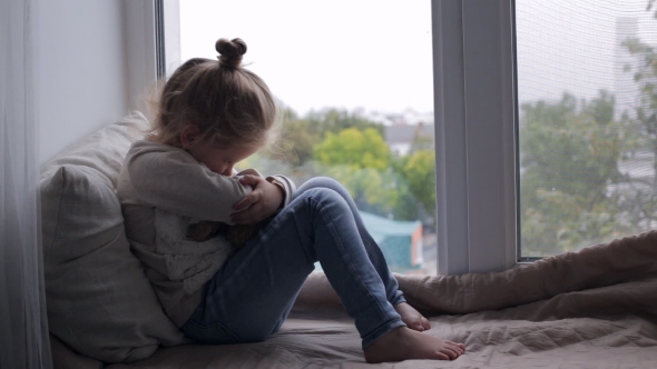 Cute Young Girl with Toy Sitting on a Window Sill