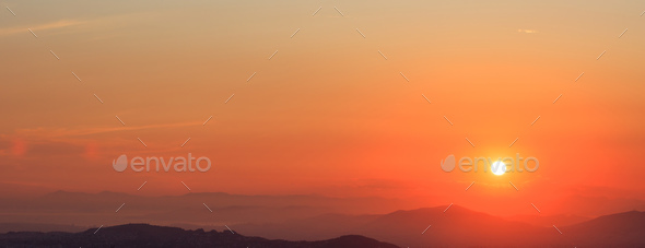 Beautiful sunset on sky over mountains background. The sun is on the right side.