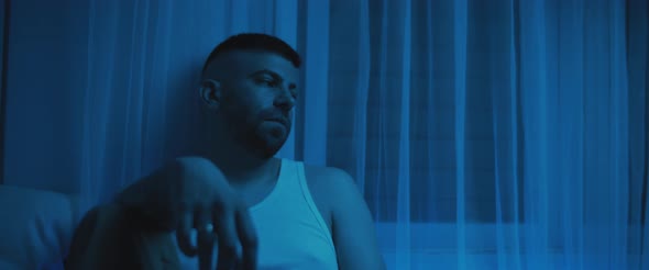 An adult depressed man sitting in the bedroom, staring to nowhere alt