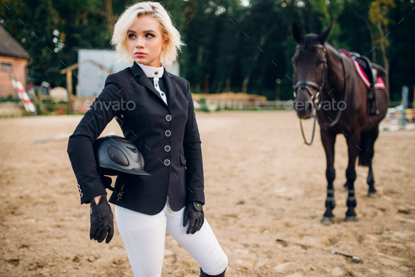 Woman with helmet in hands poses against horse - Stock Photo - Images