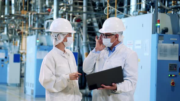 Two Factory Workers in Lab Coats are Talking alt