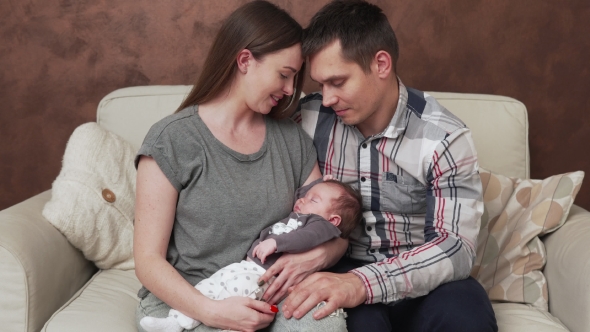 Happy Family with Newborn Baby on Sofa at Home