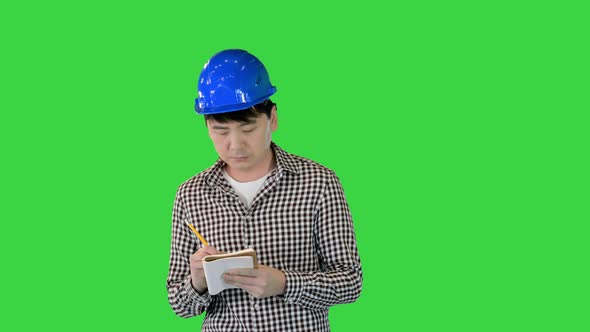 Construction Worker in a Hardhat Takes Some Notes While Walking on a Green Screen Chroma Key