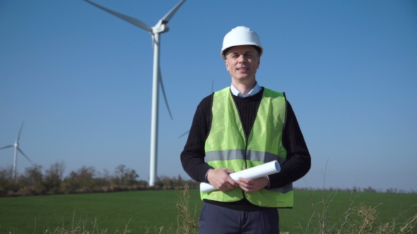 Smiling Engineer Standing Against Wind Farm alt