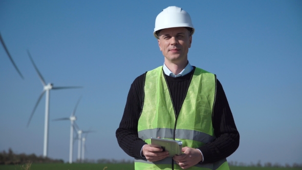 Smiling Engineer Standing Against Wind Farm alt