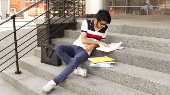 Portrait of a Happy Male Asian Student Sitting on Stairs and Reading Book