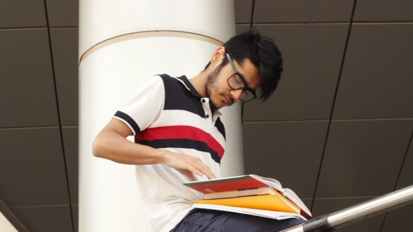 Portrait of a Happy Male Asian Student Sitting on Stairs and Reading Book