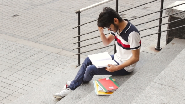 Portrait of a Happy Male Asian Student Sitting on Stairs and Reading Book