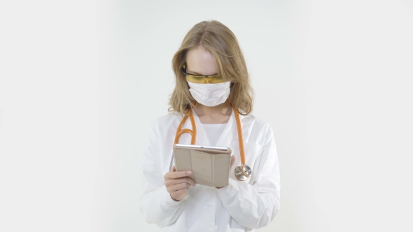 Young Female Doctor with Mask and Stethoscope Using Tablet
