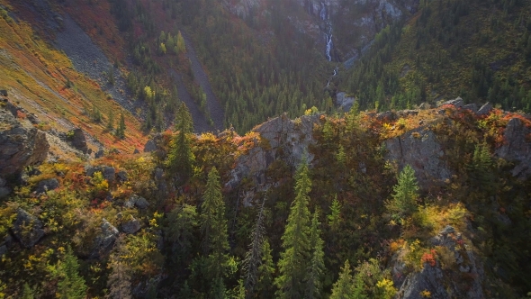 Aerial Shot of a Small Waterfall Flowing in Canyon with Autumn Mountain Forests
