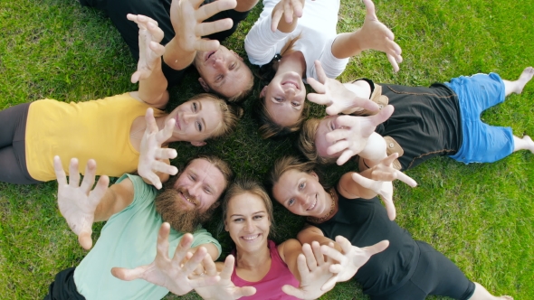 Happy Friends Lying on Grass and Waving Hands alt
