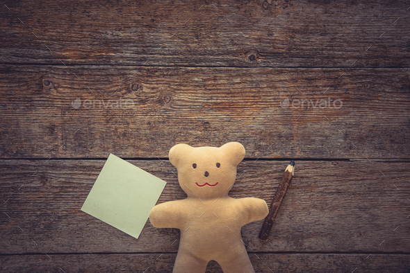 Adorable teddy bear holding sticky note and pencil on wooden table. Space for text