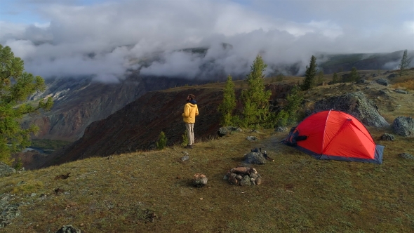 Aerial Footage of a Man Standing Near a Tent in Front of Mountain Valley.