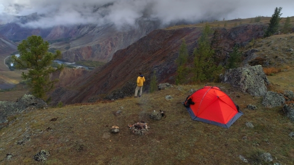 Aerial Footage of a Man Standing Near a Tent in Front of Mountain Valley,