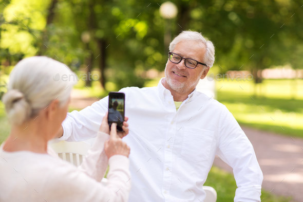 old woman photographing man by smartphone in park