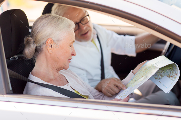 happy senior couple with map driving in car