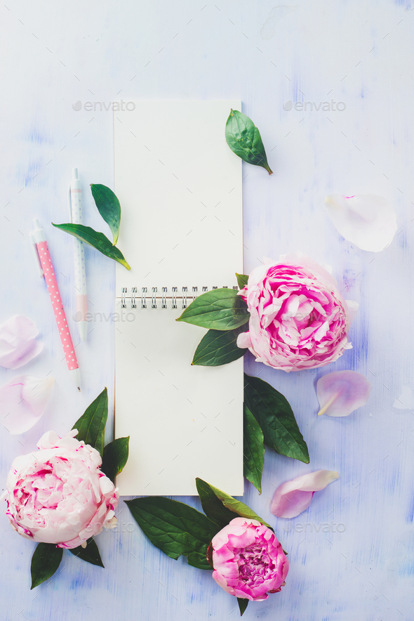 Minimal styled flat lay with peony flowers, petals and blank notebook on a white background