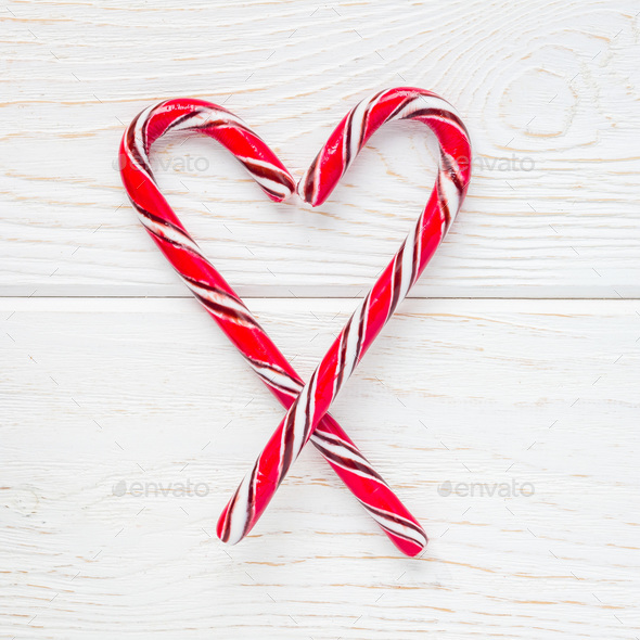 Crossed peppermint candy canes on a white wooden background, top view