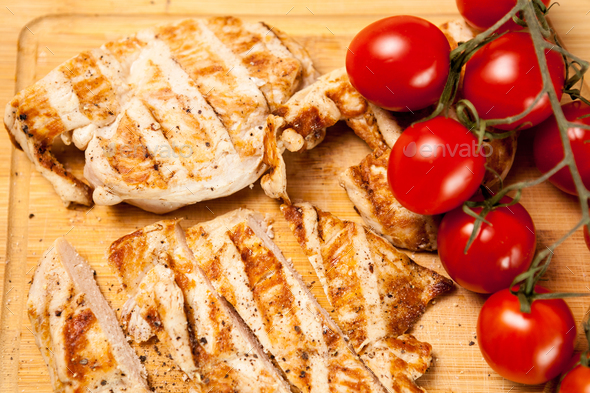Fresh grilled chicken breast on wooden board next to tomatoes