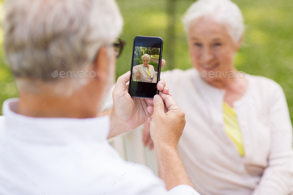 old woman photographing man by smartphone in park