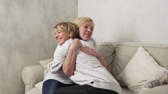 Happy Elderly Mother and Adult Daughter Hugging on Sofa