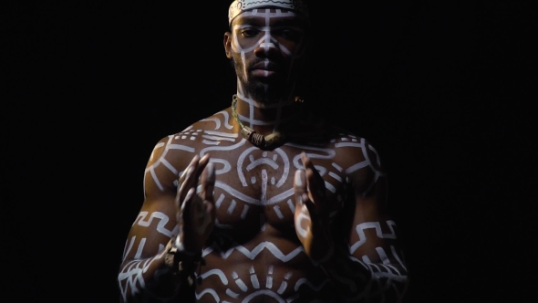 A Black Man in White Patterns and a Ritual Hat Praying on a Black Background, alt