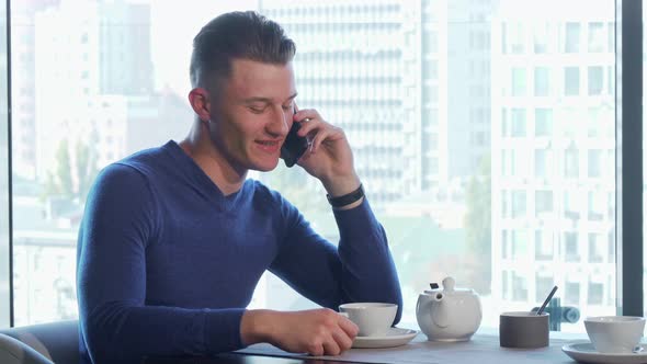 Handsome Man Enjoying Drinking Tea and Talking on the Phone at the Restaurant alt