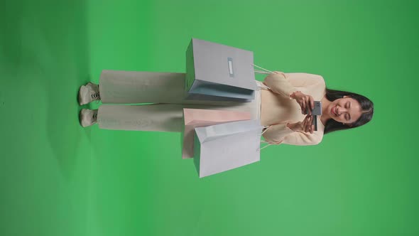 Full View Of Asian Woman With Shopping Bags And Credit Card Using Mobile Phone At Green Screen alt