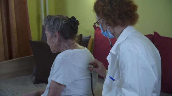 Elderly Female Doctor in White Lab Coat Medical Mask Makes Medical Examination of Senior Woman at alt