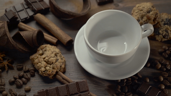 Cup of Hot Coffee with Cinnamon Sticks, Chocolate Slices and Cookies on Wooden Table alt