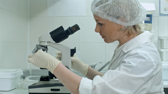 Researcher putting on gloves and using a microscope in a laboratory