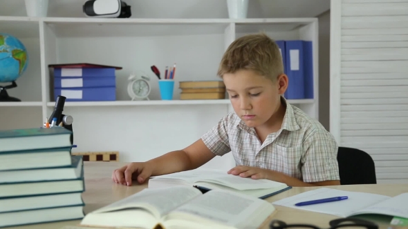 Boy Leafing Through Pages and Reading a Book Sitting at Desk alt