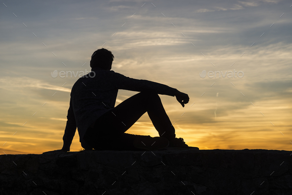 Silhouette of a seated man against a sunset sky
