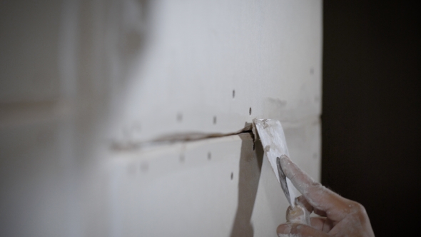 Hand of Repairman with Putty Knife Is Applying Paste on a Joint of Drywall alt