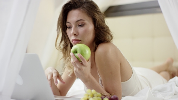 Young Woman Surfing the Internet on Her Laptop and Holding Apple