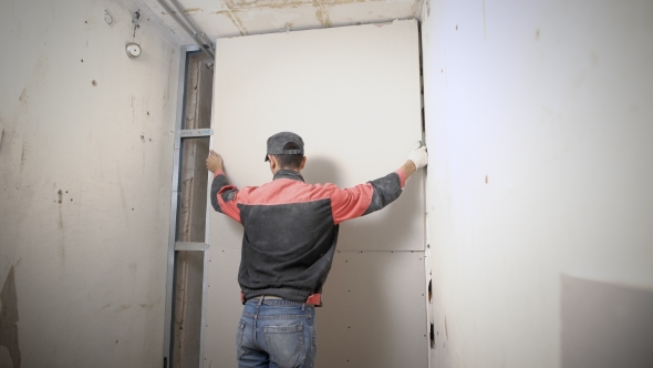 Man Is Lifting Up and Adjusting a Plasterboard on an Aluminum Construction alt