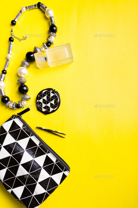 Woman handbag with makeup and accessories on yellow background. Flat lay.
