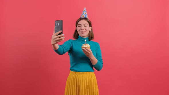 Young Woman Blowing Out Candle on Cake While Is Talking Online with Her Friends alt