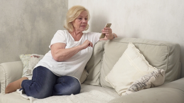 Happy Elderly Woman Sitting on Sofa and Using a Smartphone