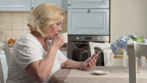 Happy Elderly Woman Drinking Coffee and Using Smartphone