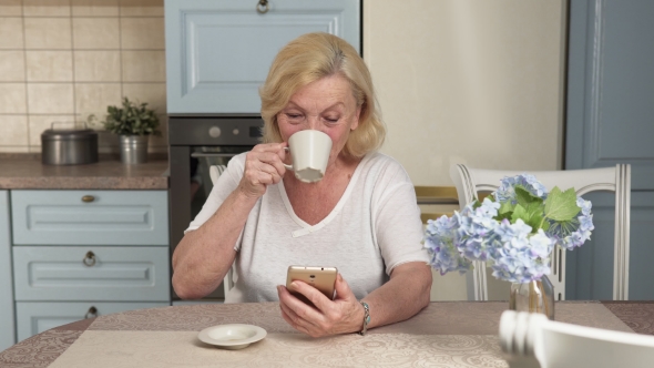 Happy Elderly Woman Drinking Coffee and Using a Smartphone